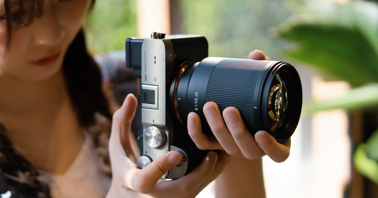 A person holds a silver and black mirrorless camera with an 85mm f/1.8 lens attached.