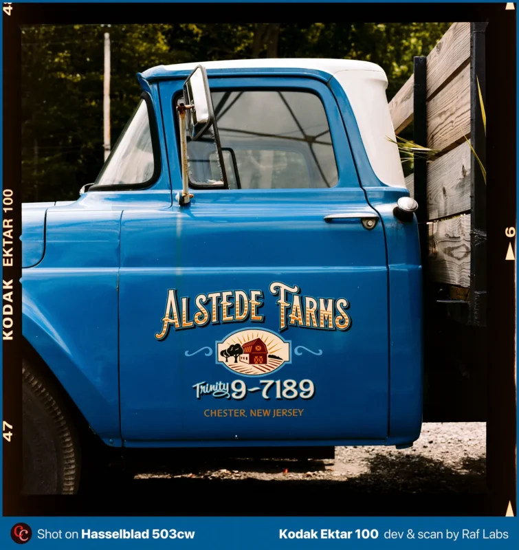 A blue vintage pickup truck with a white roof features the text "Alstede Farms" and "Trinity 9-7189" painted on its door.