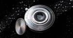 A silver Brightin Star 28mm f/2.8 lens with a detached circular metal lens cap, resting on a black, glittery surface.