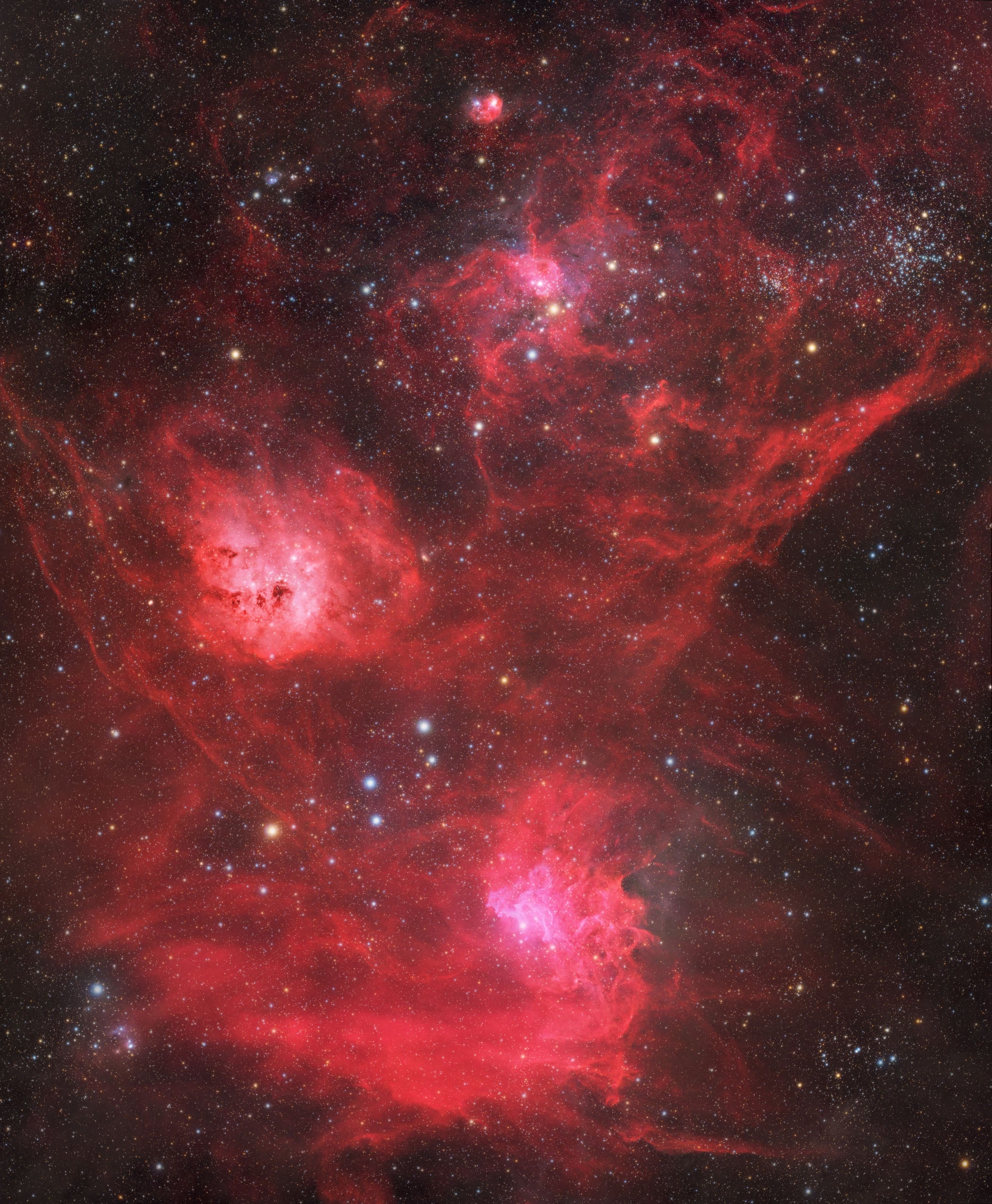 A vast, vibrant red emission nebula fills the frame, featuring glowing gas clouds, dark dust lanes, and scattered star clusters.
