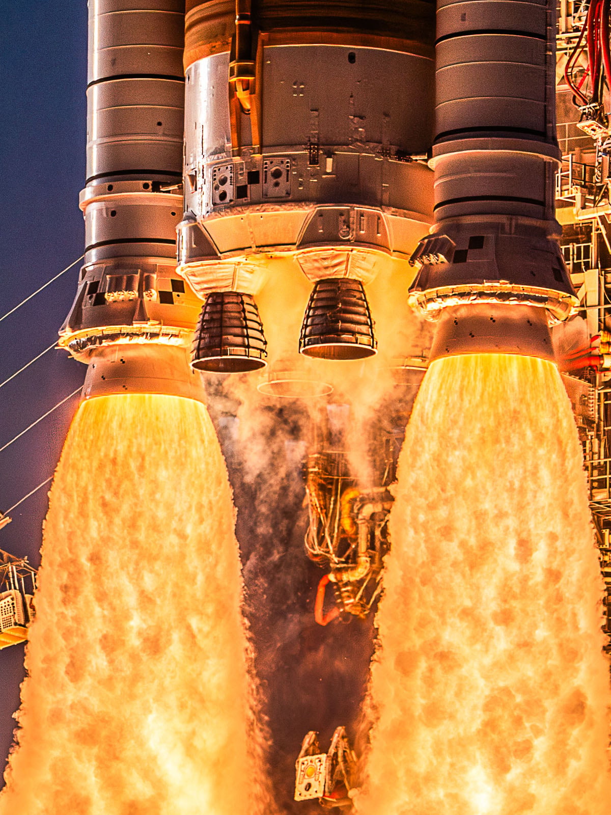 The base of a large rocket launching with bright orange flames erupting from its engines.