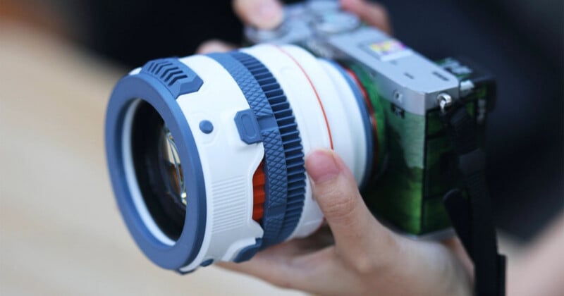 A person holds a camera with a white and blue custom-designed lens and a green patterned body wrap.