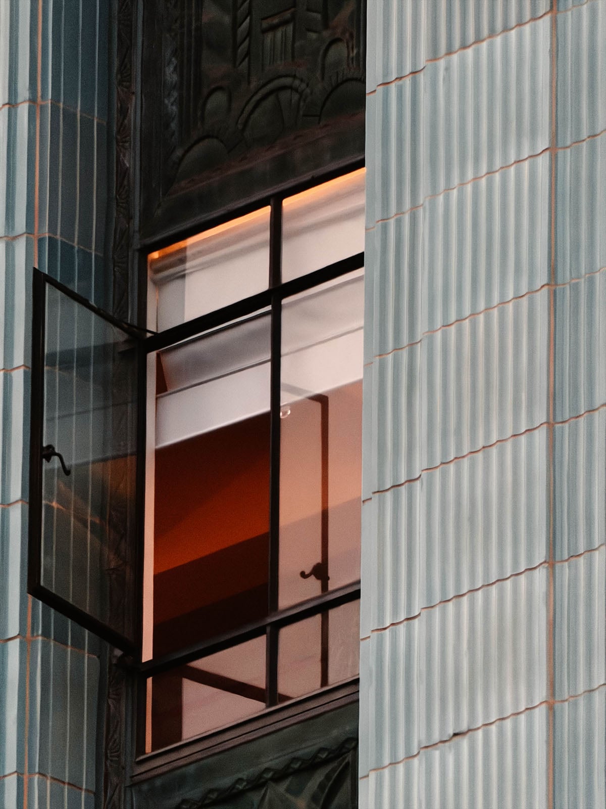 A partially open metal-framed window is set into a building facade featuring vertical, light-blue fluted tiles.