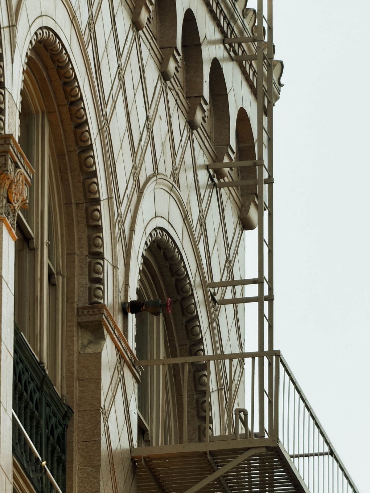 A low-angle view of a historic building facade featuring arched windows, decorative stone molding, and a metal fire escape.