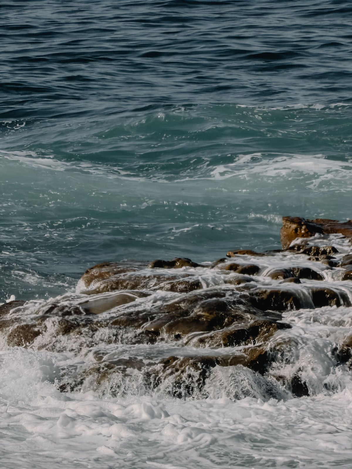 Ocean waves crash against a dark, textured rock formation jutting out from the water.