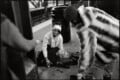 A woman kneels on a subway platform to assist a person lying on the ground, while a man in a fur coat stands nearby.