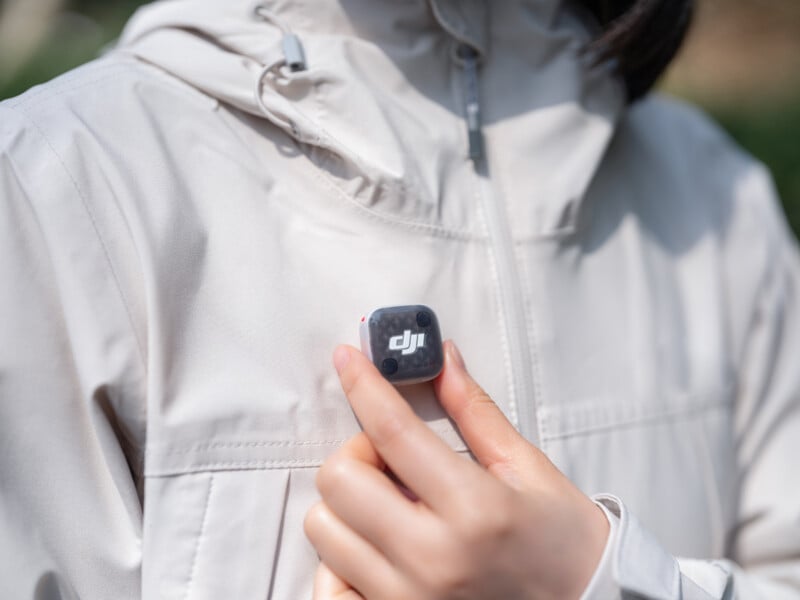 A person wearing a light-colored jacket holds a small, square device with a DJI logo on their chest.