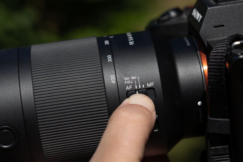 A person's finger adjusts the focus limiter switch on a camera lens, which is set to the "FULL" position.