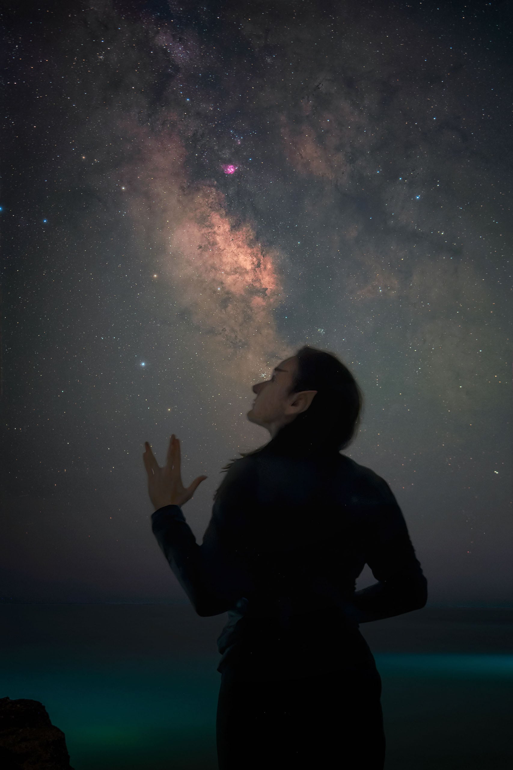 A silhouette of a person with pointed ears stands against a starry night sky, reaching a hand toward the Milky Way.