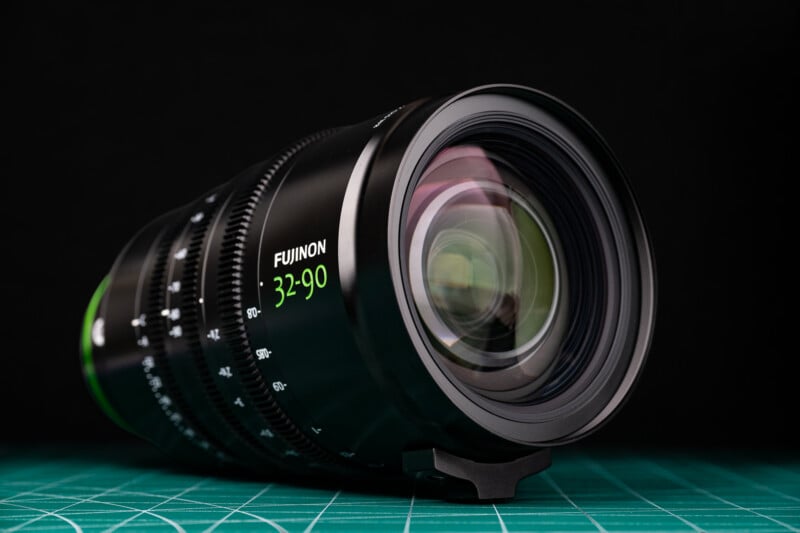 A black Fujinon 32-90 cinema lens sits on a green cutting mat against a black background.