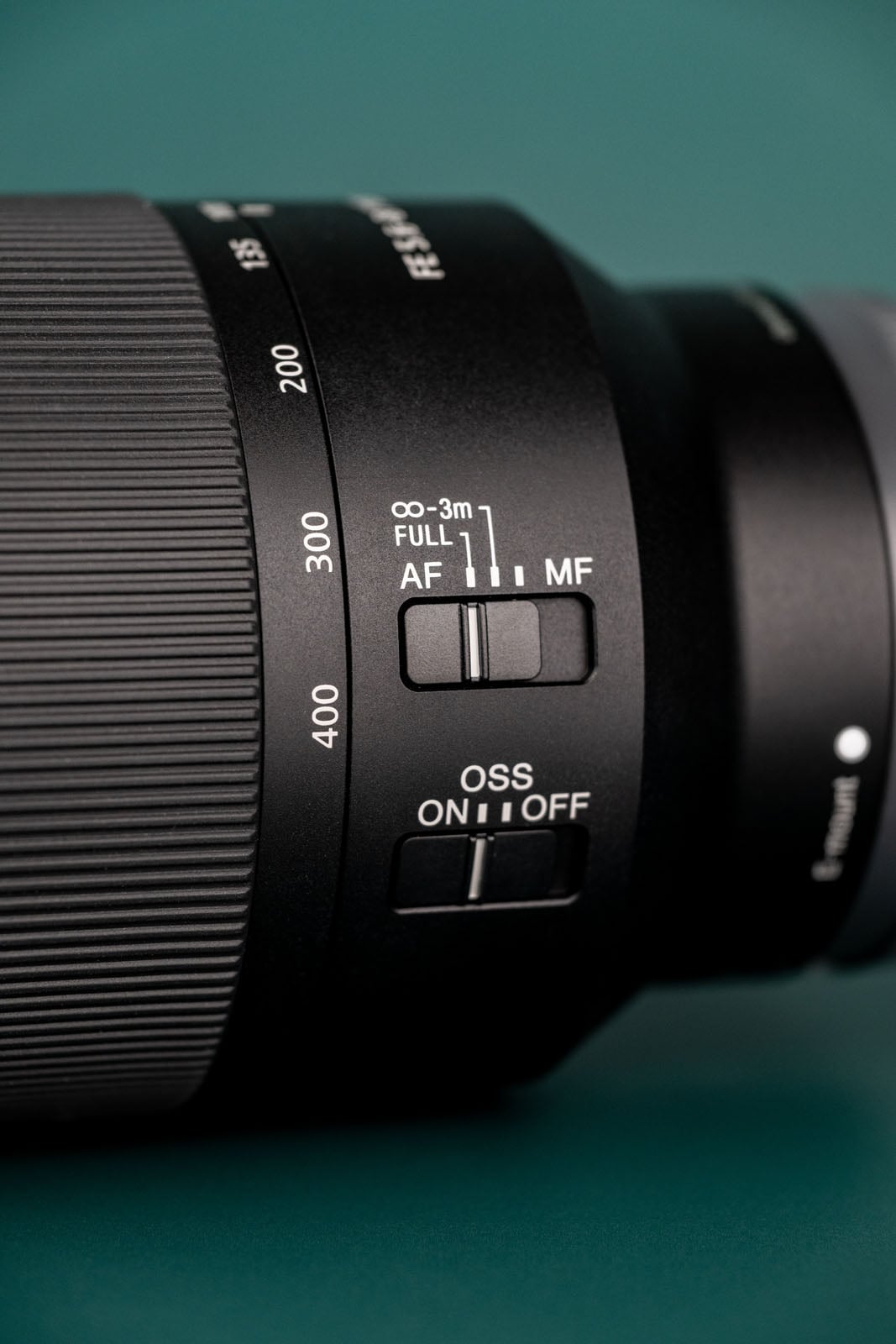 A close-up of a camera lens barrel showing focal length markings from 135 to 400, a focus limiter switch, and an optical steady shot switch.