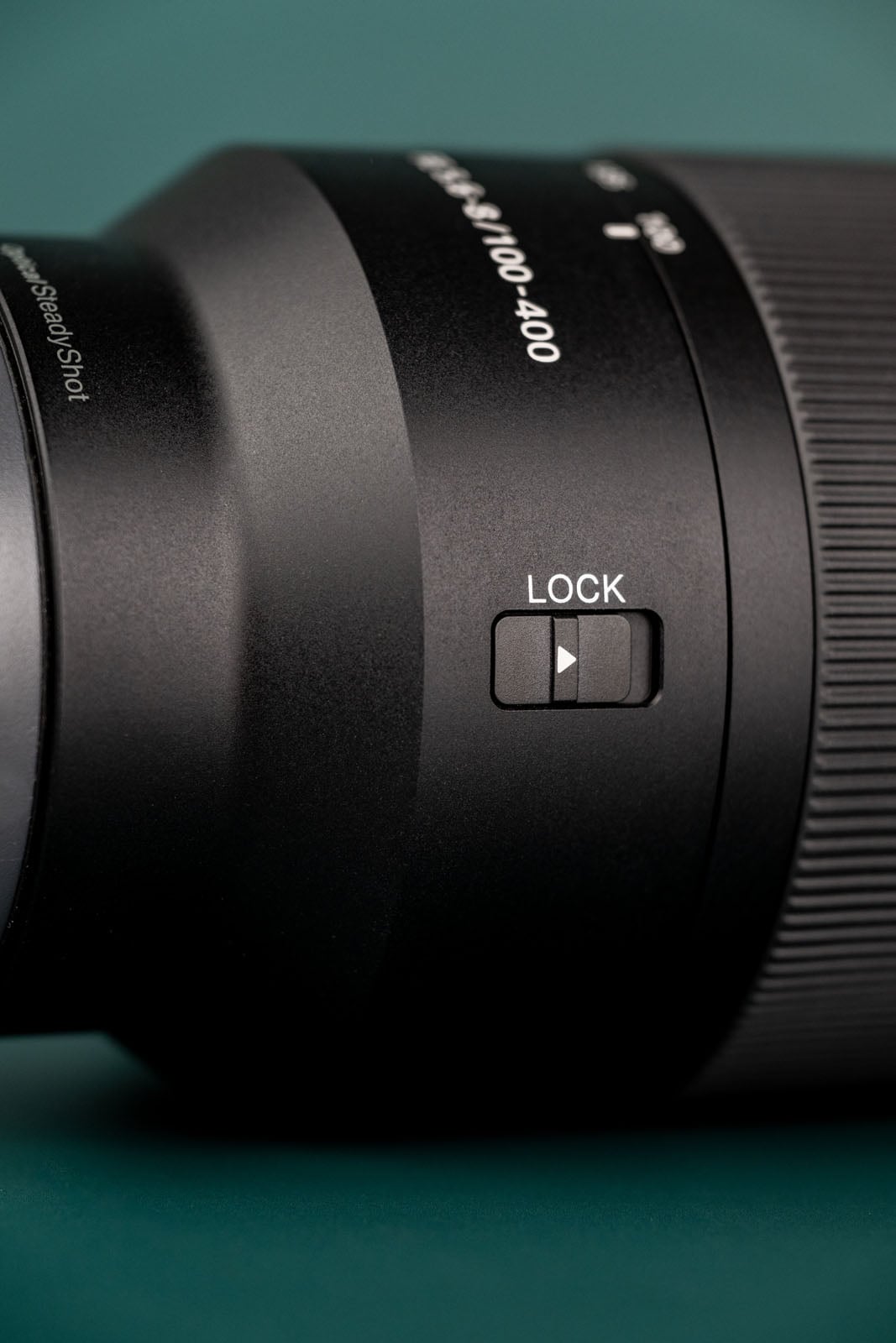 A close-up of a camera lens barrel featuring a zoom lock switch and text reading 4.5-5.6/100-400 and Optical SteadyShot.