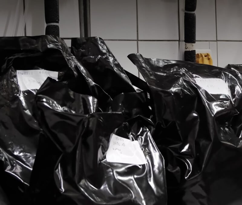 Several black plastic bags with handwritten labels are stacked against a white tiled wall.