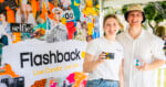 A young woman and man stand in front of a colorful collage backdrop branded 