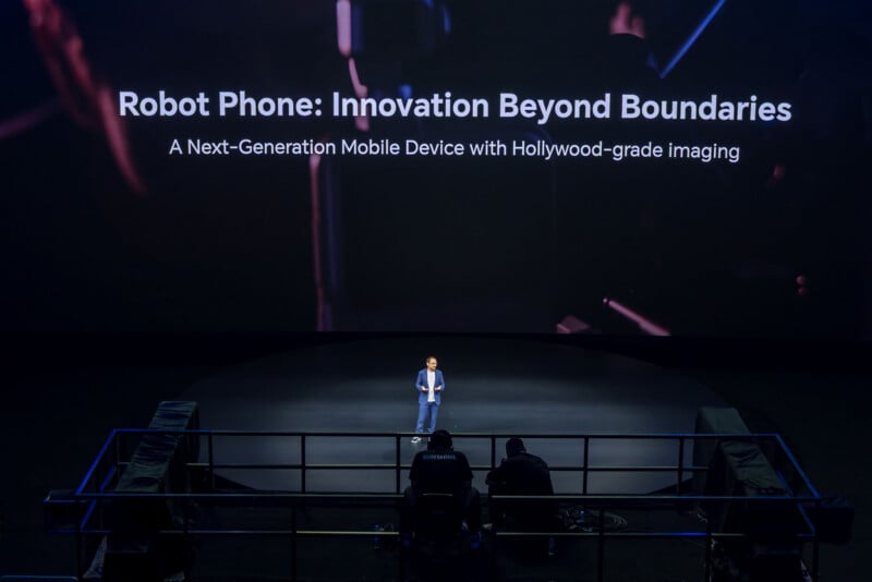 A man in a blue suit stands on a stage in front of a large screen displaying the text "Robot Phone: Innovation Beyond Boundaries.