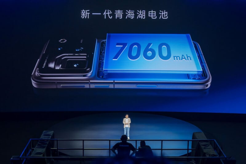 A presenter stands on a stage in front of a large screen displaying a smartphone with a 7060 mAh battery and the text "新一代青海湖电池".