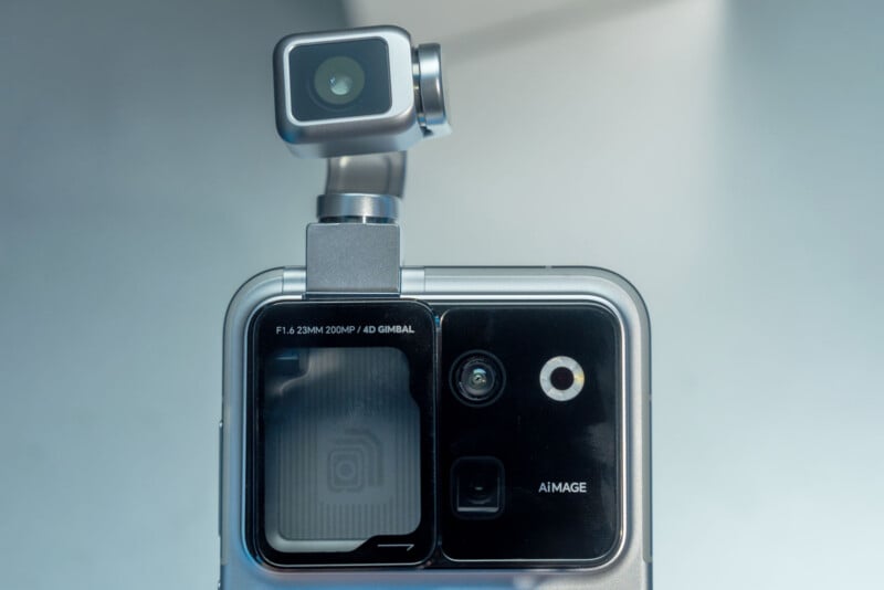 A close-up of a smartphone back panel featuring a prominent, silver-colored gimbal-mounted camera module extending from the top, alongside a secondary camera array labeled "F1.6 23MM 200MP / 4D GIMBAL" and "AiMAGE".
