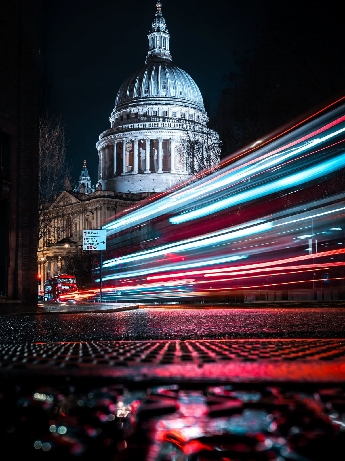 A long-exposure shot of a red bus moving past St. Paul's Cathedral at night, creating streaks of red and blue light.