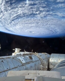 A view from the International Space Station looking down at a large, swirling hurricane over Earth's horizon.