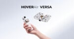 A hand holds a white handheld camera gimbal, while a white drone with a protective cage floats in the air above it, both labeled HOVERAir VERSA.