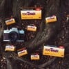 A Minolta SRT 202 camera surrounded by several boxes of Kodak Professional T-MAX 100 film on a tree root background.