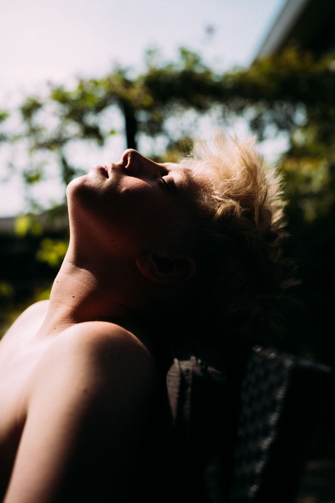 A person with short blonde hair tilts their head back in the sunlight, with their face partially in shadow.