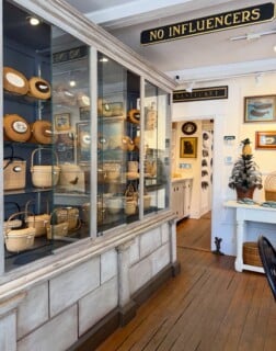 A large glass display case filled with woven Nantucket baskets stands in a shop with a sign that reads 