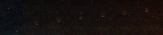 A series of eight faint, glowing circular objects are arranged in a horizontal line against a dark, grainy background.