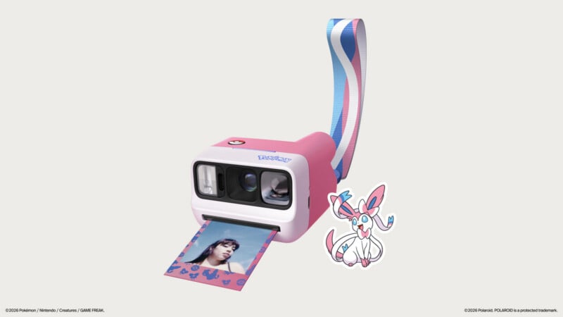 A pink and white Polaroid-style instant camera featuring Pokémon branding, a Sylveon-themed wrist strap, and a printed photo showing a person, accompanied by a Sylveon sticker.