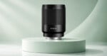 A black camera lens labeled "AF 85/1.8" stands upright on a circular, light green pedestal against a matching curved background.