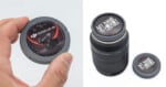 A hand holds a gray camera body cap with a DJI Ronin 4D-8K sticker, next to a camera lens with a custom 