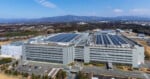 An aerial view of a large, multi-story Sony industrial facility with solar panels on the roof and a parking lot in the foreground.