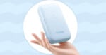 A hand holds a light blue, rectangular Godox device against a light blue background with a wavy pattern.