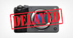 A front-facing view of a gray digital camera body with a lens mount and a red, distressed 