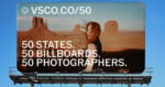 A billboard against a blue sky features a woman with windblown hair standing in a desert landscape with rock formations, with the text 