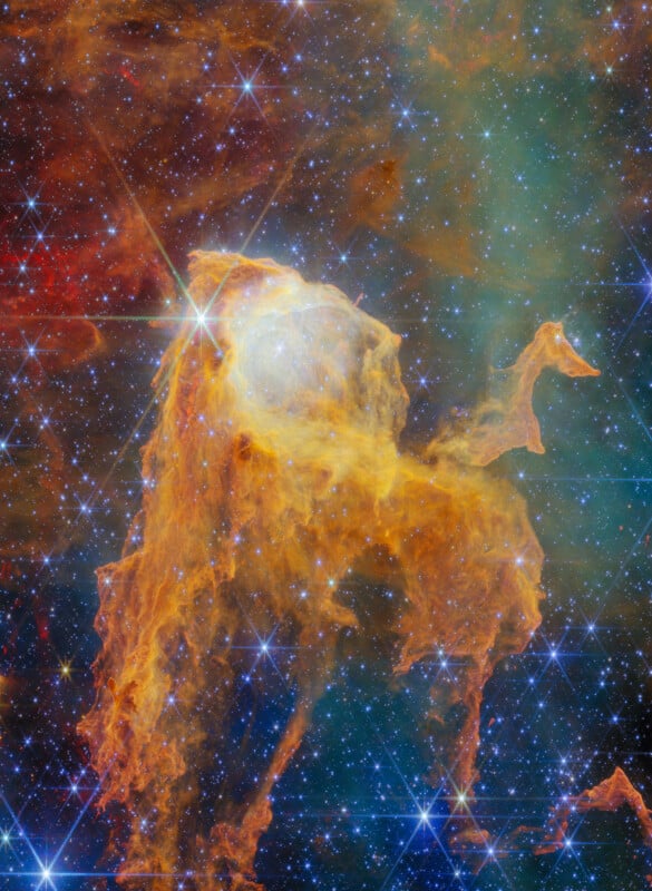 A dense, golden-orange nebula of gas and dust glows against a dark, star-filled background, featuring a bright star with prominent diffraction spikes.