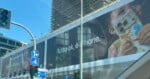 A large billboard displays an advertisement featuring a child holding a messy iPhone with the text