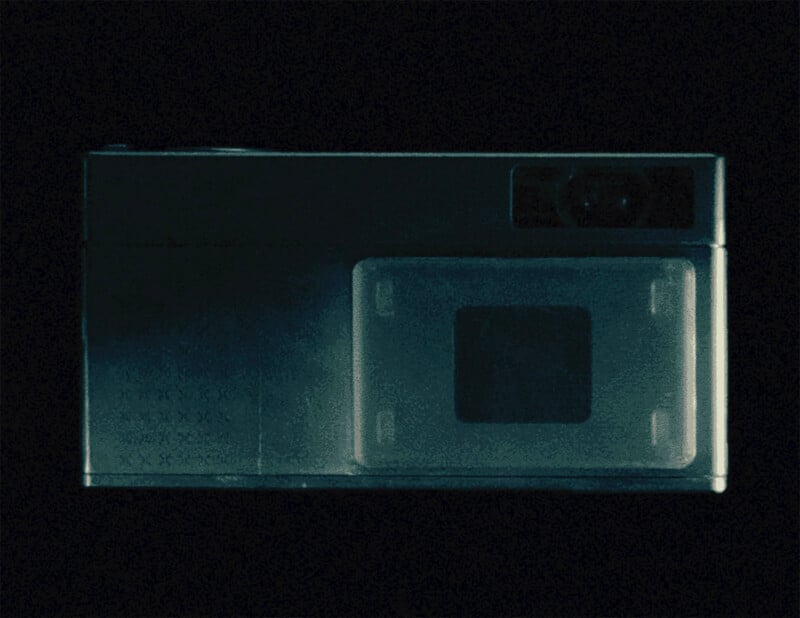 A dark, rectangular camera with a prominent square lens housing and a small viewfinder window against a black background.