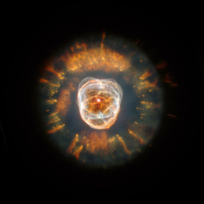 The Clown Face Nebula features a bright, glowing central star surrounded by complex, shell-like layers of orange and blue gas.