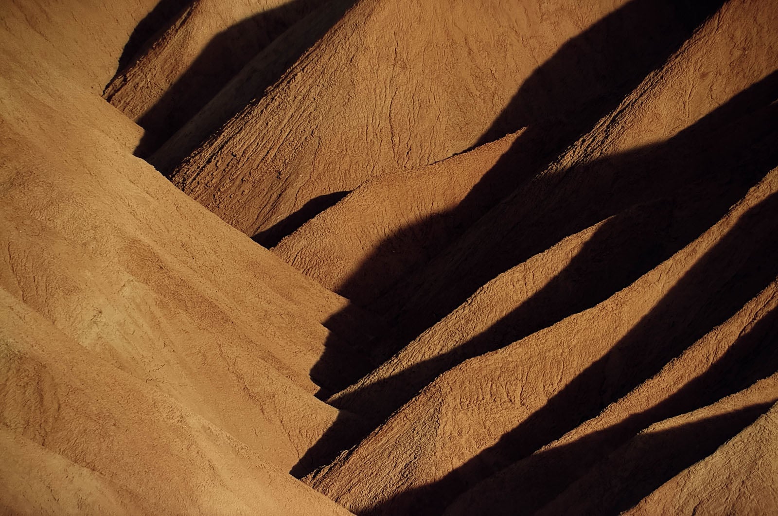 Deep, angular shadows cast across the textured, golden-brown slopes of arid, eroded hills.