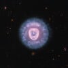 A glowing, spherical nebula with a bright, pink, heart-shaped inner structure sits centered against a dark background of distant stars and galaxies.