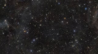 A dense field of stars and distant galaxies scattered across a dark, vast expanse of space.