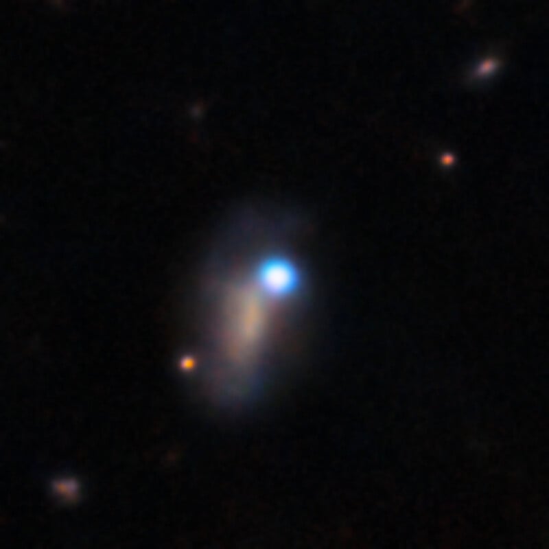 A bright blue star-like object sits atop a faint, elongated, brownish-grey galaxy against a dark space background.