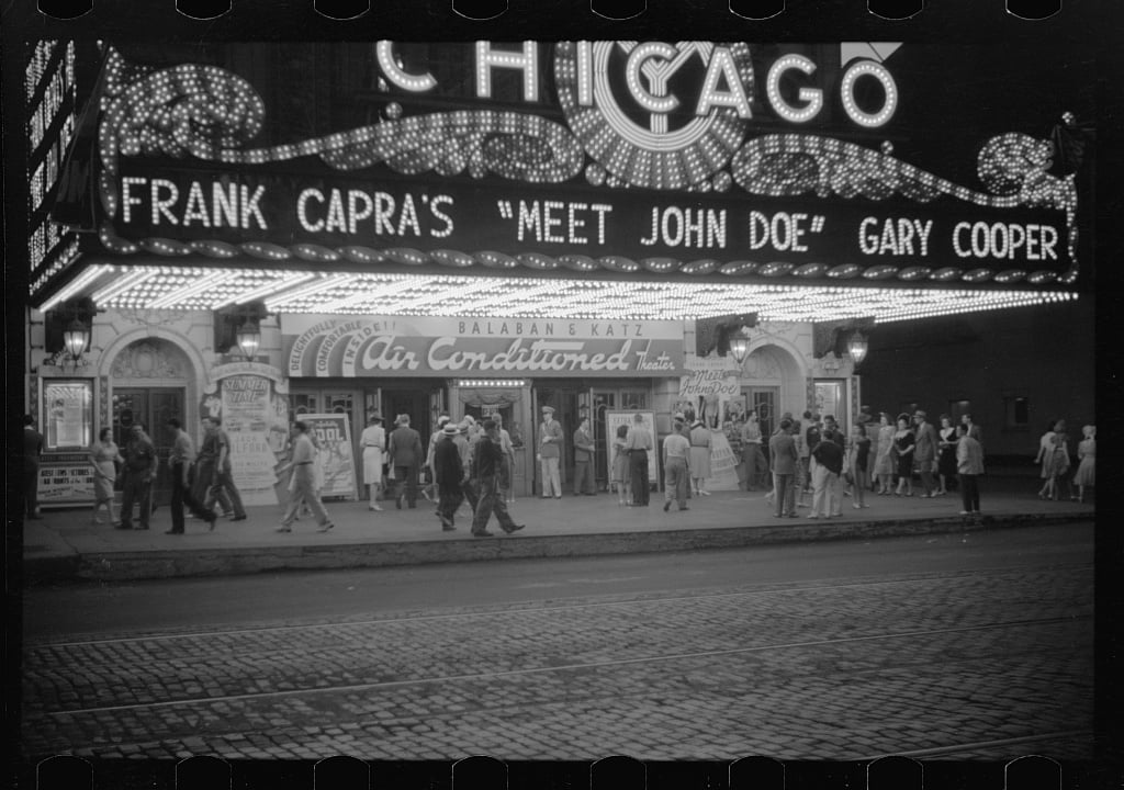 People walk along the sidewalk in front of the Chicago Theater, which displays a marquee for the film Meet John Doe starring Gary Cooper.