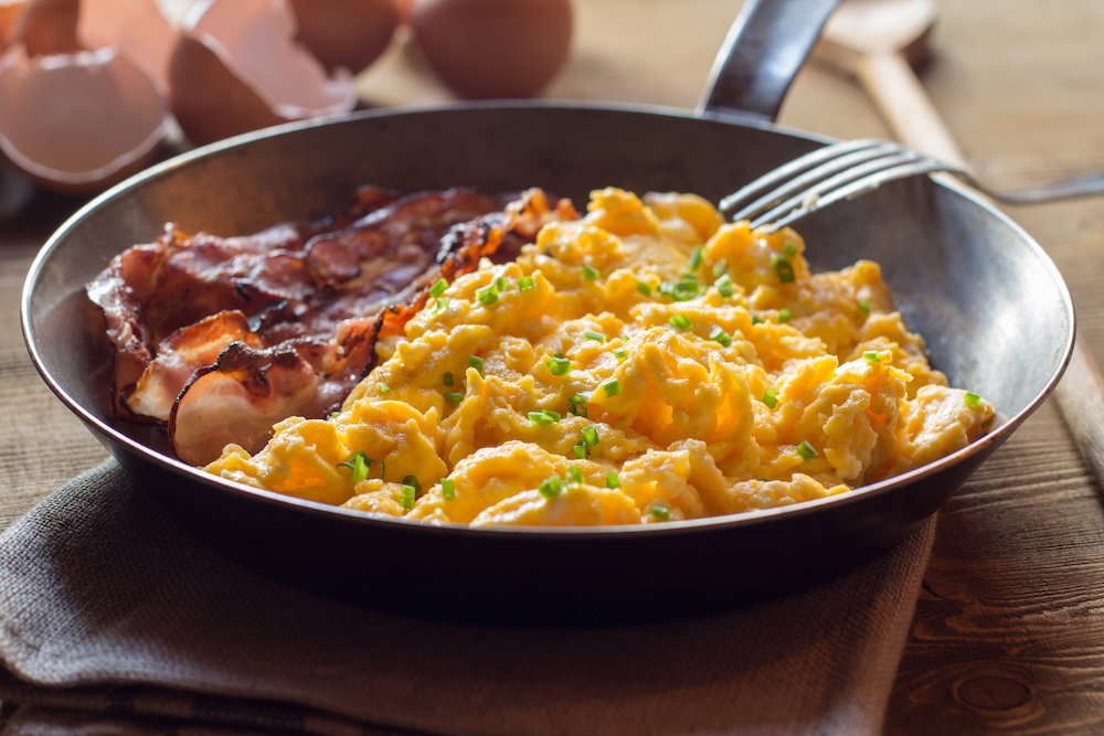 Close up of scrambled eggs with bacon in frying pan