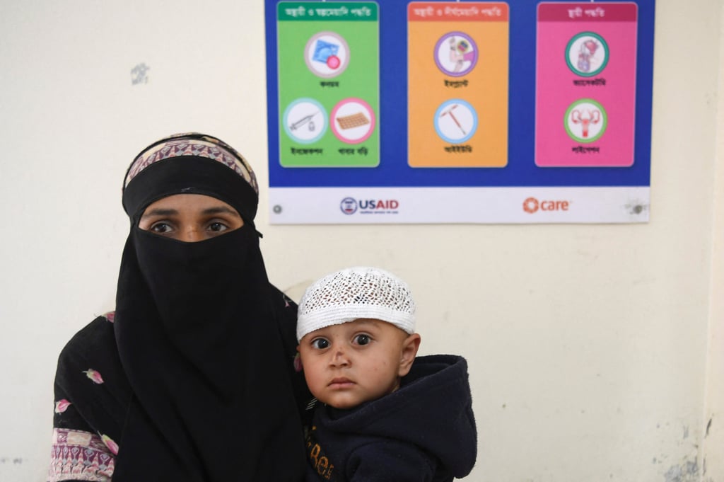 A mother and child look on as a USAID-funded health awareness poster hangs behind them at a health complex in Kishoreganj, Bangladesh, on Monday. Photo: Reuters