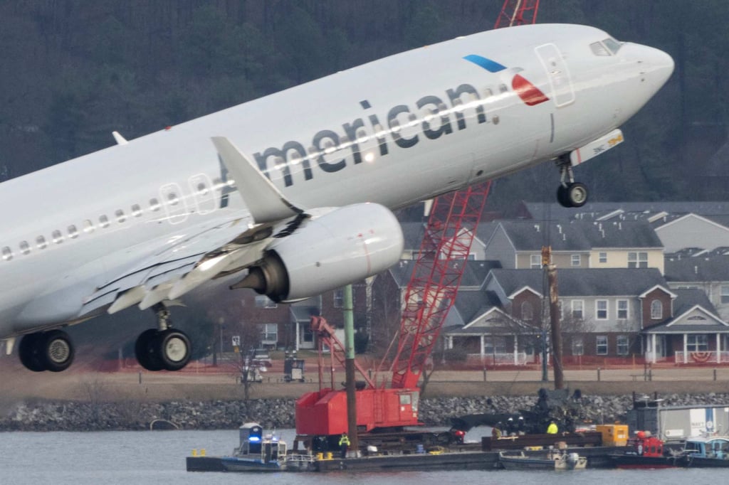 Recovery teams lift the mangled remains of a military helicopter that crashed mid-air with an American Airlines commercial aeroplane from the Potomac River as an American Airlines plane passes by on February 6. Photo: AFP