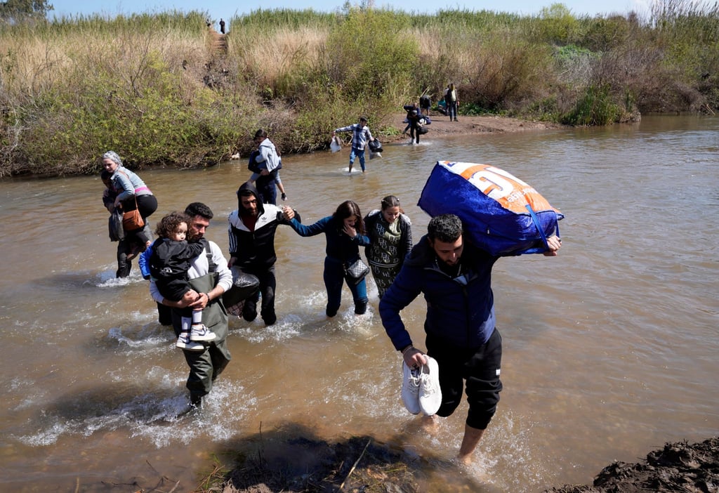 Syrian families who fled clashes in Syria cross a river marking the border between Syria and northern Lebanon. Photo: AP