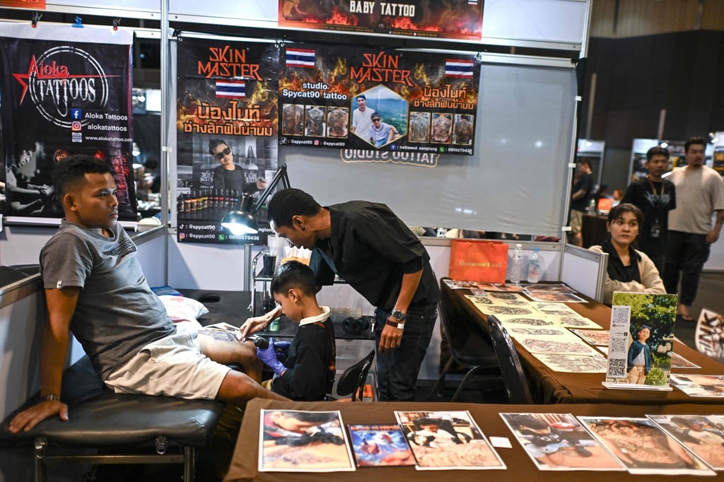 Nine-year-old Napat Mitmakorn, a Thai child tattoo artist, works on his uncle’s tattoo with his father, Nattawut Sangtong (right), at the 2025 Thailand Tattoo Expo in Bangkok. Photo: AFP