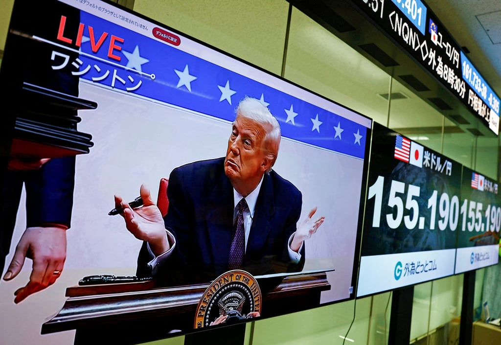Live footage showing US President Donald Trump during the signing ceremony for his executive orders, next to screens displaying the dollar-yen exchange rate at a dealing room of Gaitame.com in Tokyo on January 21, 2025. Photo: Reuters.